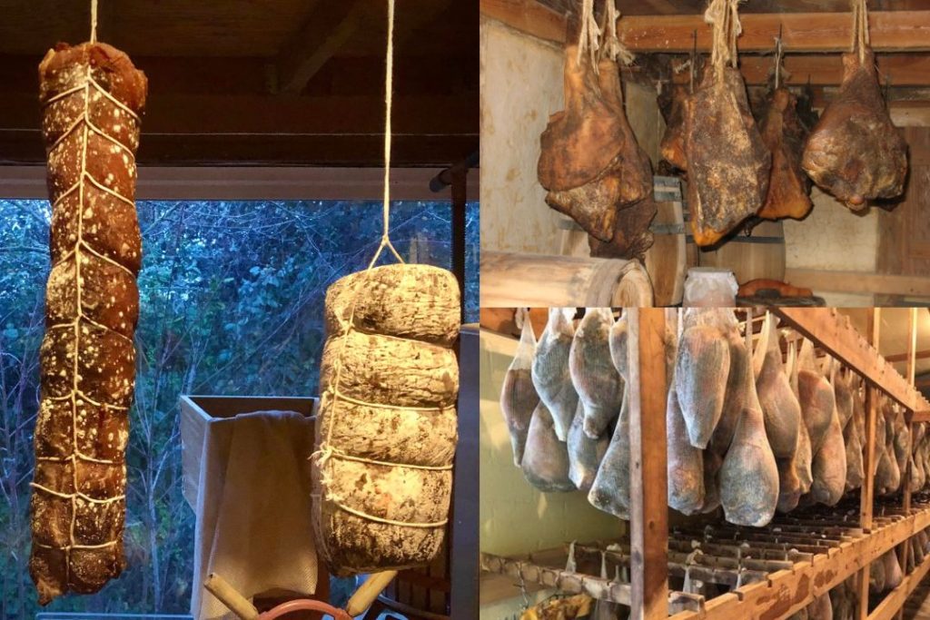A row of country hams wrapped in white cheesecloth bags hanging from wooden hooks in a dim brick-walled aging room